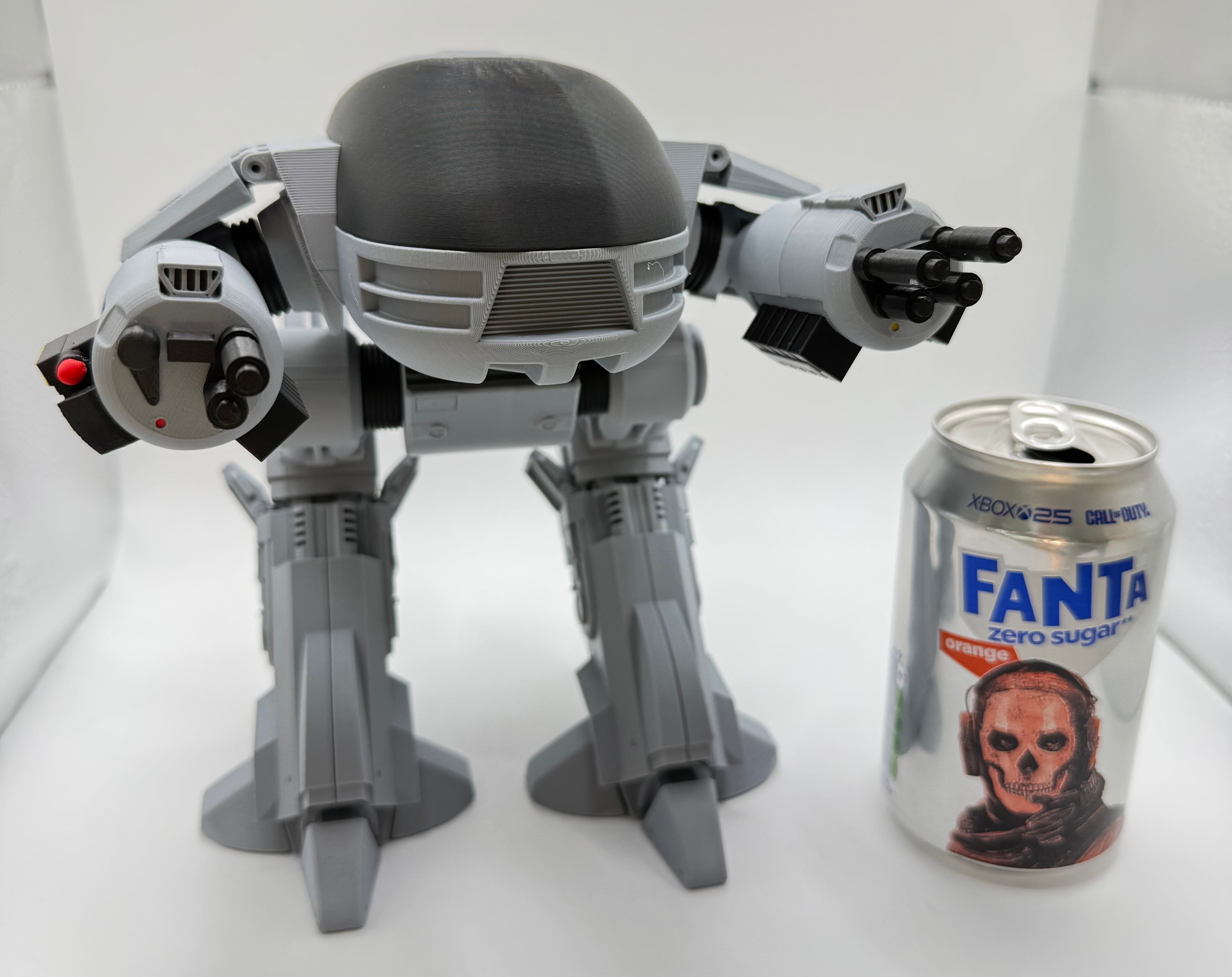 Gray ED209 robot model next to a can of Fanta on a white background