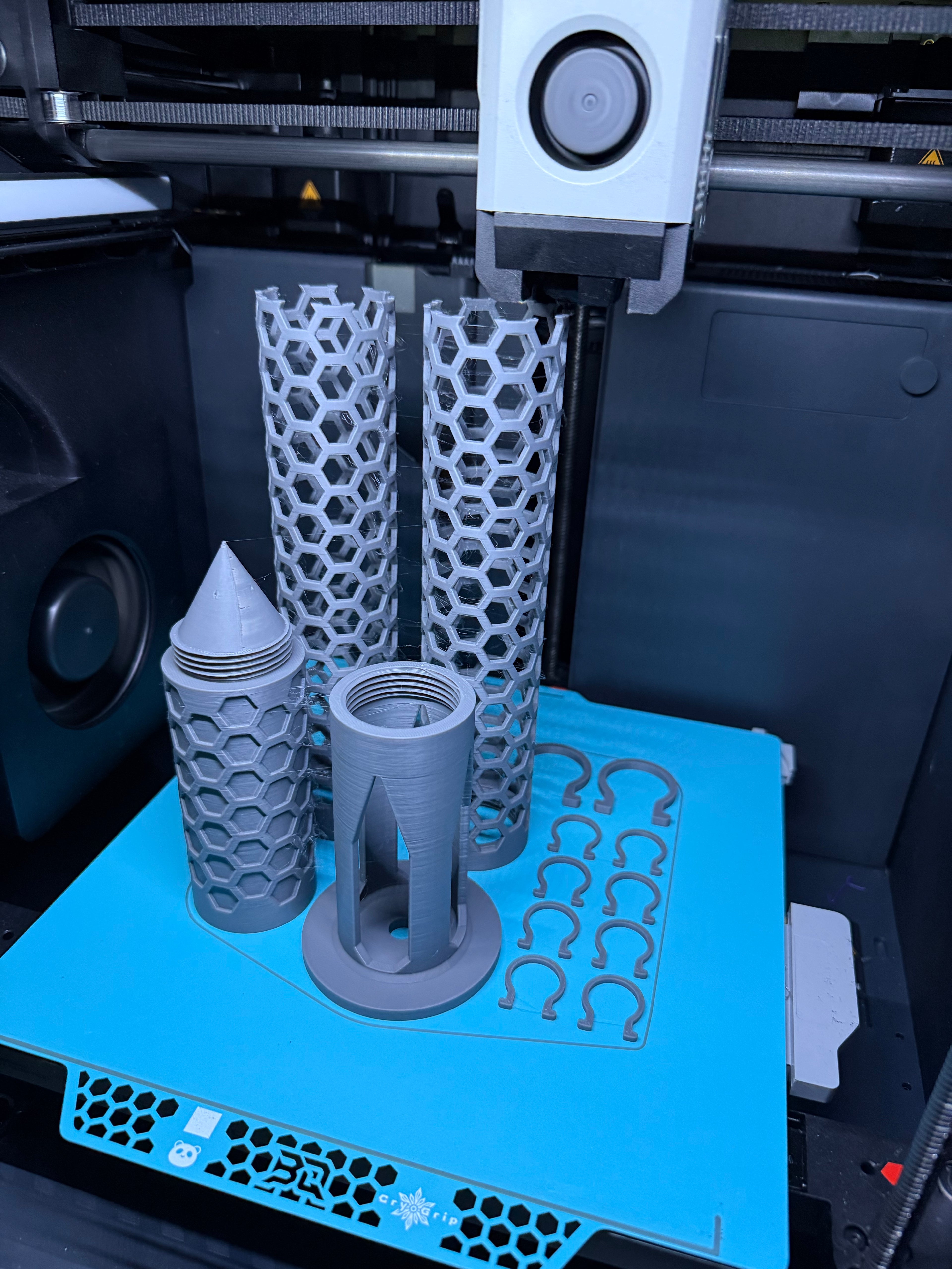 Freshly 3D printed Modular Moss Pole Kit parts on the printer bed, including poles, spike base, water reservoir and clips