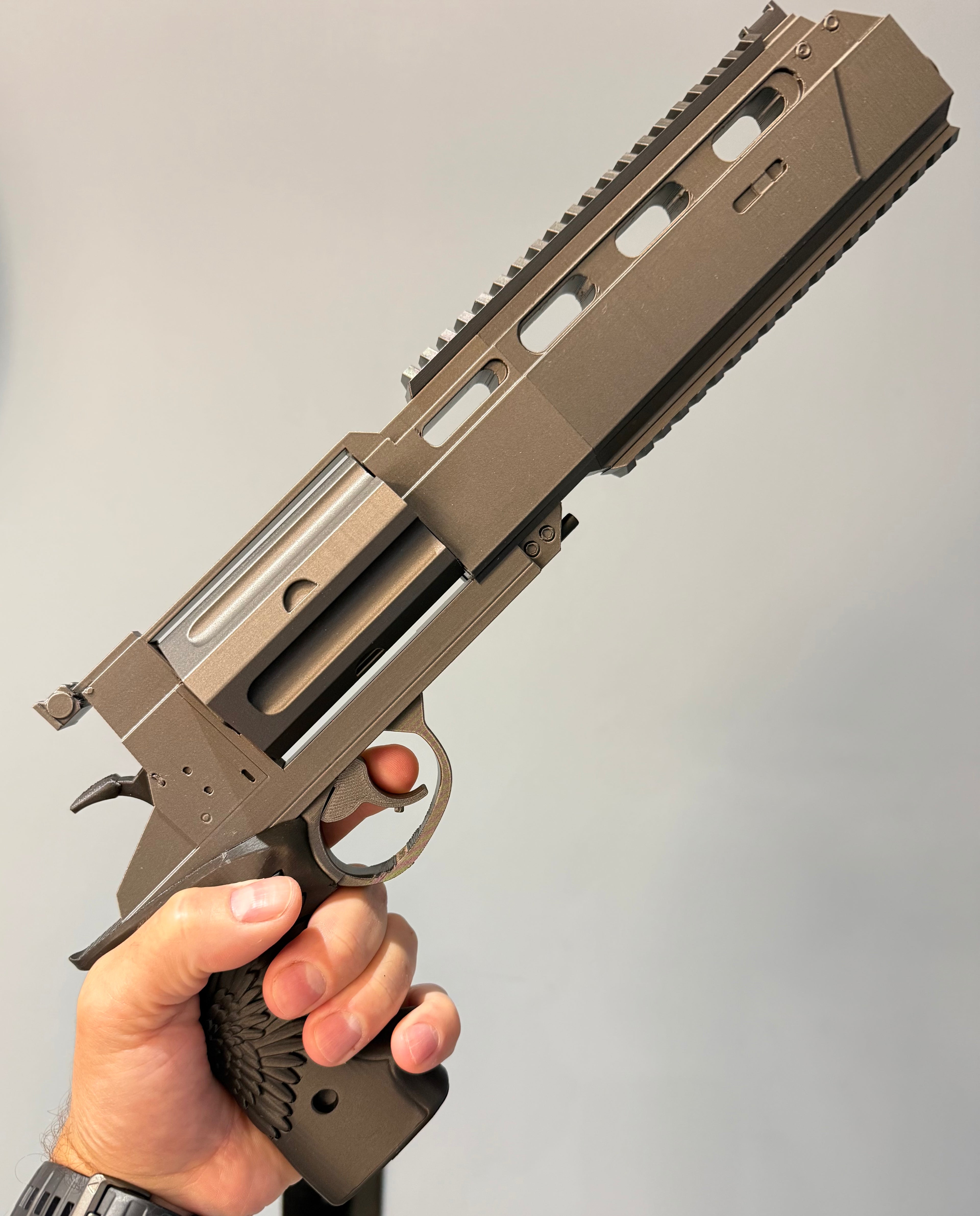 A hand holding a compact, modern pistol with a matte metallic finish and a textured grip, shown against a plain light gray background. Leon's Magnum Revolver – Resident Evil Requiem Prop Kit