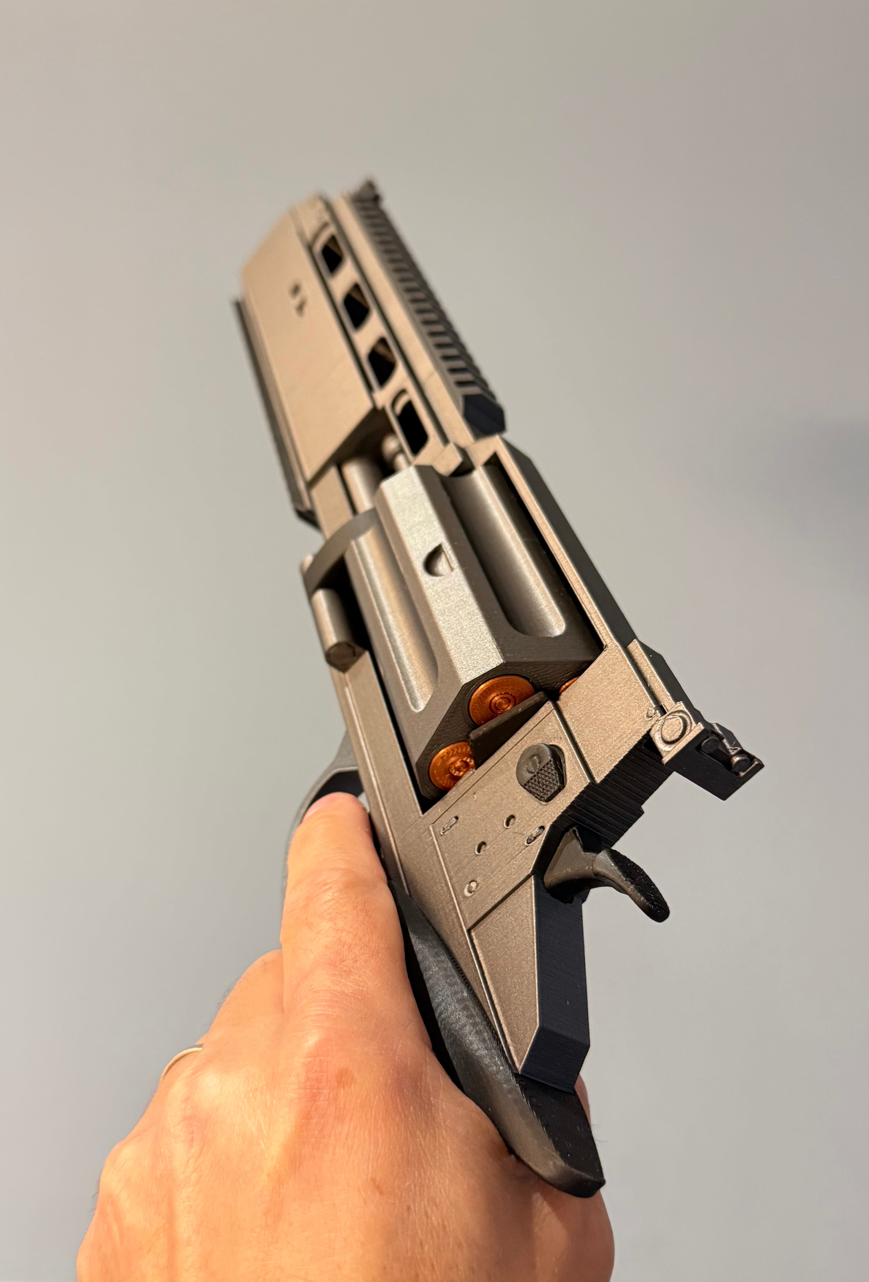 A hand holding a metallic silver and black revolver-style pistol with orange accents against a plain light gray resident evil background.
