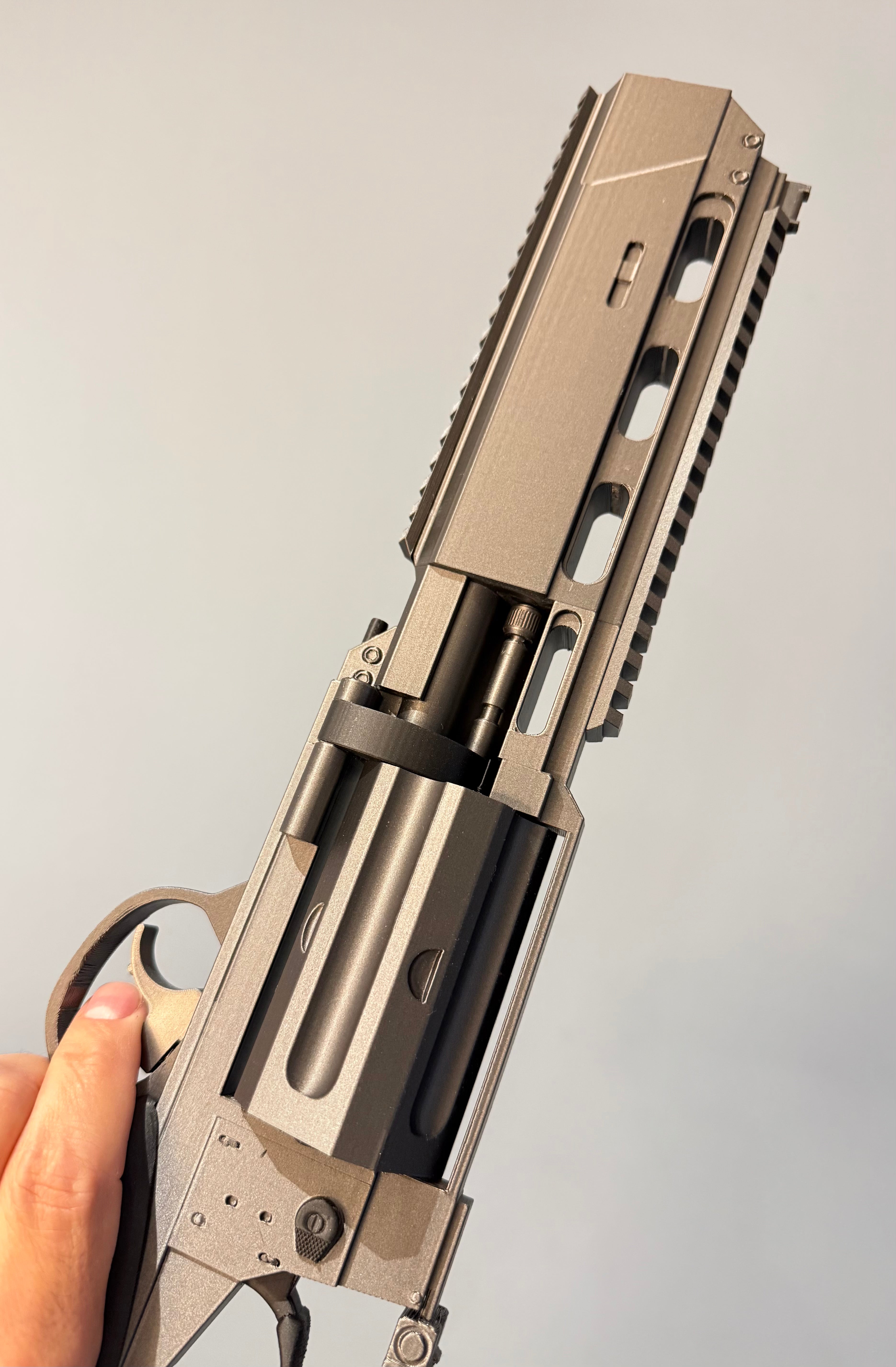 A close-up of a metallic silver and black rLeon's Magnum Revolver – Resident Evil Requiem Prop Kit held by a person's hand against a plain light gray background.